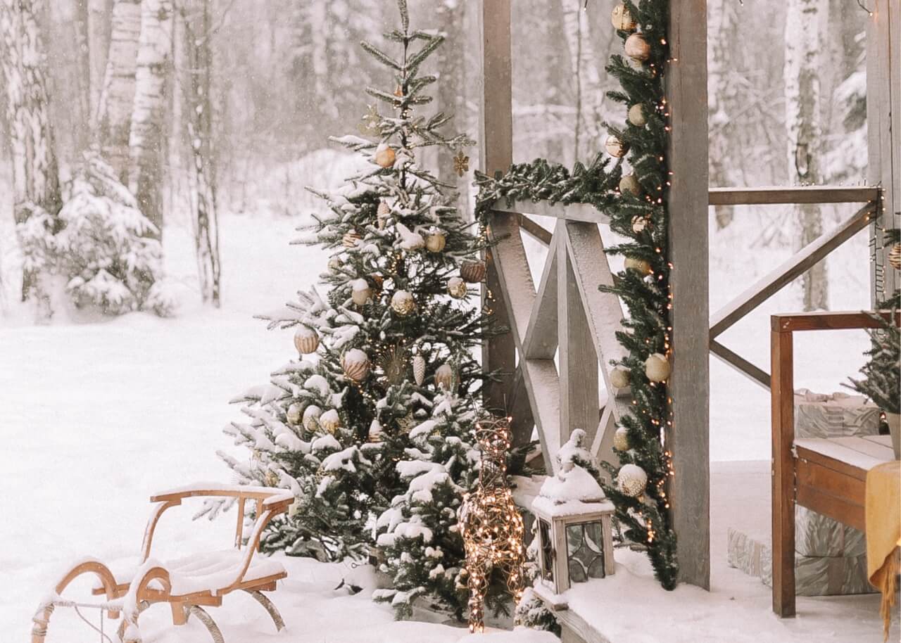 Winter snowy wonderland display on porch with tree, sled and forest in the background.