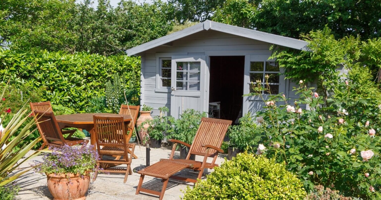 shed in flower garden with table and chairs in front